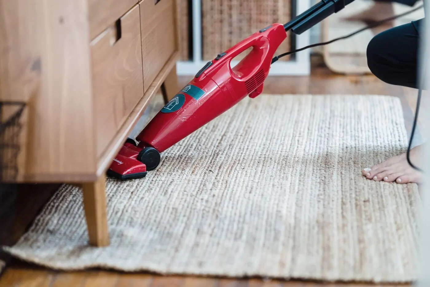 Stock photo of a red vacuum cleaning a woven rug under a wooden cabinet