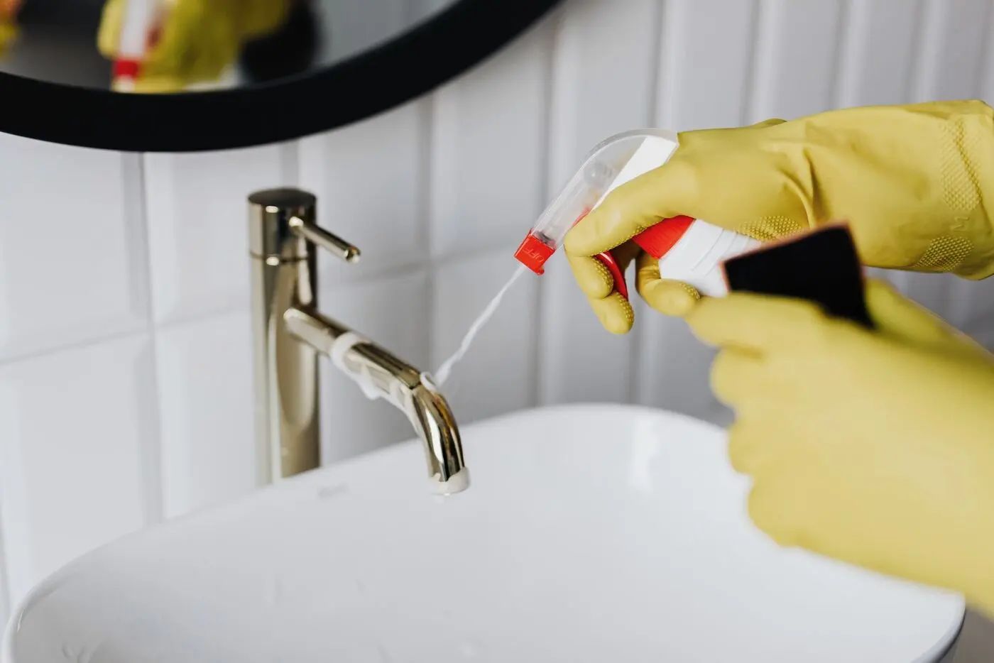 Stock photo of gloved hands spraying cleaner on a bathroom faucet