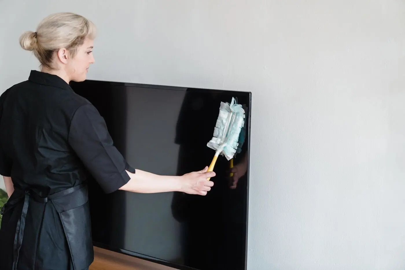 Stock photo of a cleaner dusting a television screen with a duster