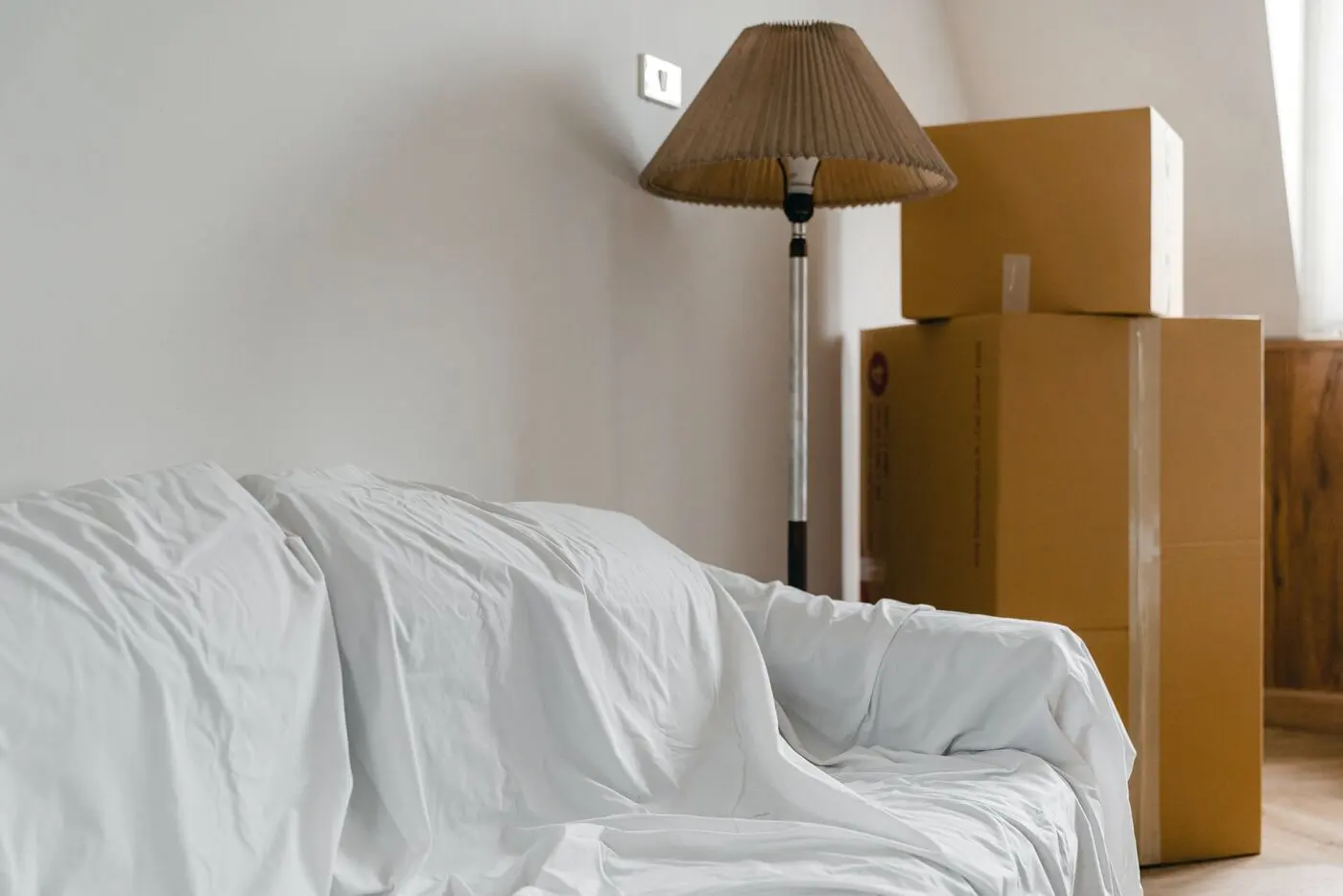 Stock photo of packed moving boxes and a sheet-covered sofa in a bright room